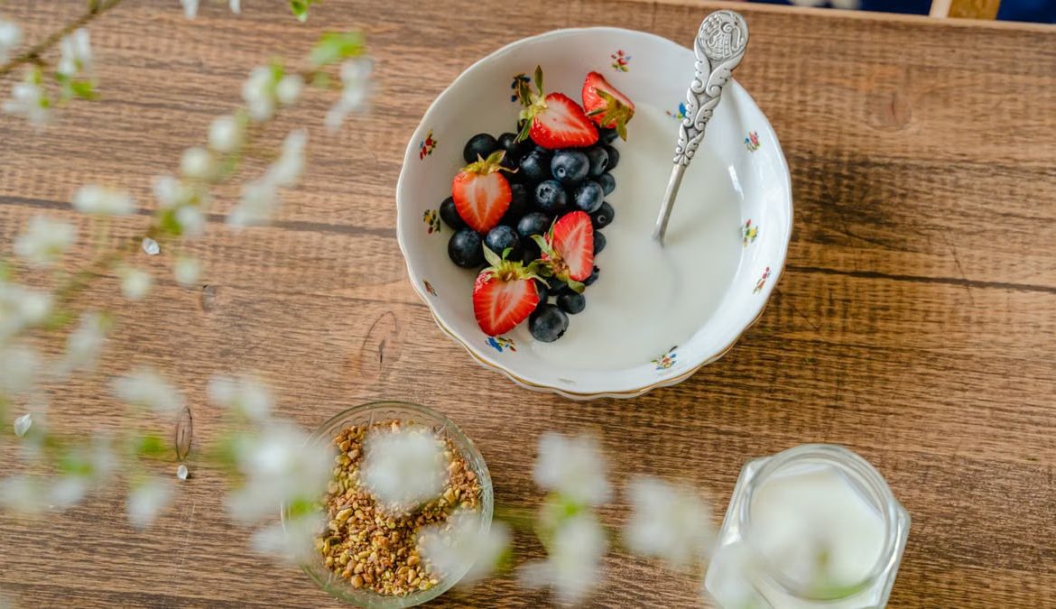 A bowl of fresh strawberries, blueberries with yogurt on a wooden table, viewed from above.